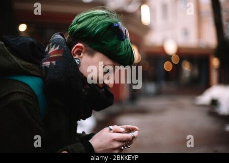 Porträt der glücklichen nicht-binären Hipster Frau mit Smartphone während auf der Bank in der Stadt sitzen Stockfoto