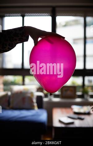 Die Hand einer Frau hält einen rosa Ballon zu Hause. Stockfoto