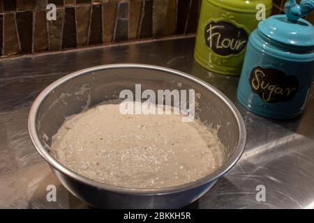 Eine Schüssel mit aufgestiegenen Teig in einer Stahlschale. Neben zwei bunten Kanistern in grün und blau. Stockfoto