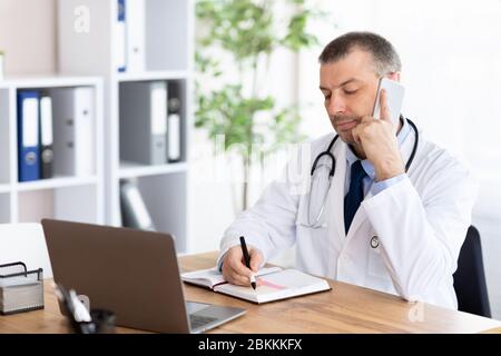 Arzt telefoniert mit seinen Patienten und schreibt Notizen Stockfoto