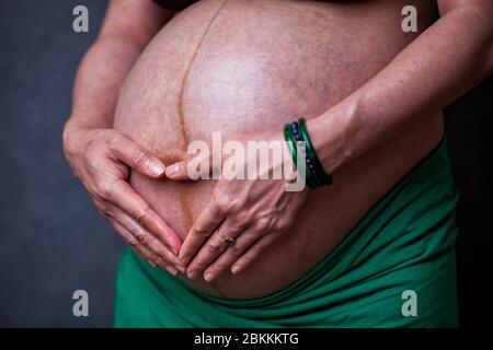 Magen einer schwangeren Frau im dritten Trimester mit den Händen über den Fötus in Form eines Herzens Stockfoto