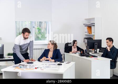 Büromitarbeiter in einem offenen Raum, verschiedene Dinge tun, Kollegen chatten, Projekte diskutieren, an PCs arbeiten, etwas Papierkram erledigen. Coworking-Kontra Stockfoto