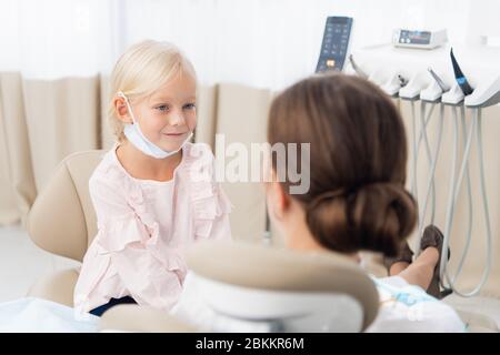 Kleines Mädchen, das im Zahnarztbüro sitzt und lächelt. Kind keine Angst vor Zahnarzt. Zahnarzt gibt dem Kind Patienten Beratung über Zahnpflege und Hygiene. Stockfoto