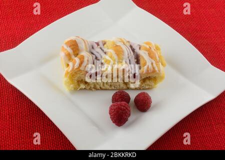 Himbeerkaffeetorte mit frischen Himbeeren auf weißem Teller auf roter Tischdecke Stockfoto