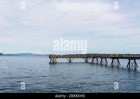 SIDNEY, KANADA - 14. JULI 2019: Menschen auf Holzsteg, der über das Meer in das Wasser mit einem bewölkten Himmel ragt. Stockfoto