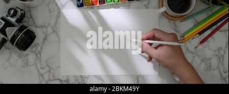 Overhead-Aufnahme von männlichen Künstler Zeichnung auf Skizzenpapier mit Malwerkzeugen auf Marmor Arbeitstisch Stockfoto