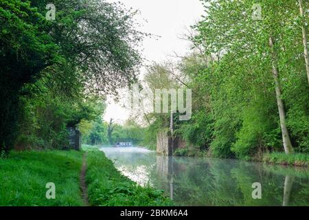 Nebel, Narrowboat und Baumspiegelungen entlang des Oxford Kanals an einem Frühlingsmorgen kurz nach Sonnenaufgang. In der Nähe von Kings sutton, Northamptonshire, England Stockfoto