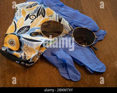 Nahaufnahme von handgefertigtem Blumenstoff-Gesichtsmask mit Sonnenbrille und Einweg-blauen Handschuhen auf einem Holztisch. Stockfoto