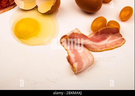 Zerbrochenes Hühnereier, Scheiben Wurst und Speck und Tomaten auf weißem Hintergrund. Nahaufnahme Stockfoto