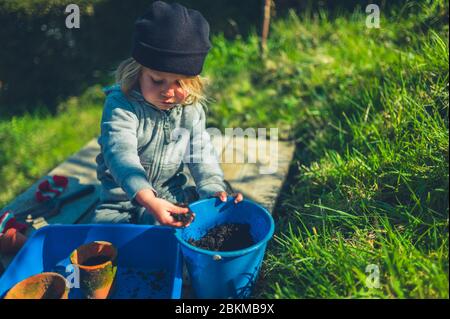 Ein kleiner Vorschulkind pflanzt an einem Frühlingstag im Garten Samen in Töpfen Stockfoto