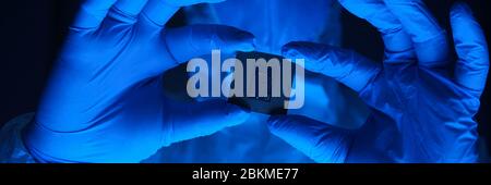 Ein Mann in einem Schutzanzug hält ein Mikrochip, der in seinen Händen. Research Lab Arbeiter Handschuhe und Schutzbrille. Stockfoto