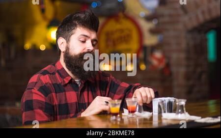 Get Drunk Concept. Mann mit betrunkenem Gesicht sitzen alleine an der Theke. Hipster in der Nähe Gläser mit alkoholischem Getränk, kurzer Cocktail. Guy verbringen Freizeit in Bar trinken Cocktail, defokussed Hintergrund. Stockfoto
