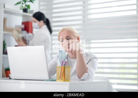 Müde Frau Arzt mit Laptop, maskierte Kollegin. Stockfoto