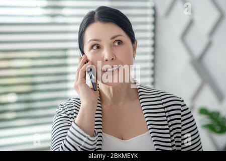 Zufriedene Brünette Frau im Gespräch auf einem Smartphone. Stockfoto