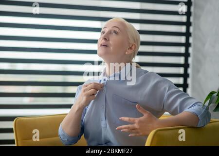 Blonde Erwachsene Frau sitzt in einem gelben Sessel. Stockfoto