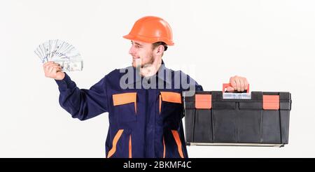 Handyman mit lächelndem Gesicht in harter Hut auf weißem Hintergrund. Service- und Zahlungskonzept. Baumeister Geld verdienen, hält der Mechaniker Bargeld, Banknoten in der Hand. Mann mit Werkzeugkasten bekam Gehalt, Geld für Arbeit. Stockfoto