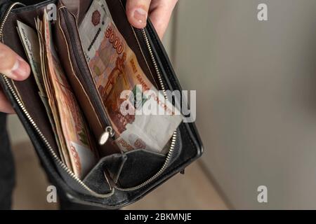 Ein Mann mit einer schwarzen Brieftasche voller russisches Geld. In einer schwarzen Brieftasche, Banknoten sind meist 5,000 Rubel pro Stück. Gehalt und Rente erhöht, Leistungen Stockfoto