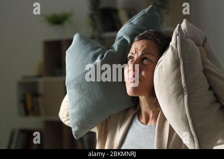 Genervte Erwachsene Frau, die nachts zu Hause im Wohnzimmer den Lärm der Nachbarn leidet Stockfoto