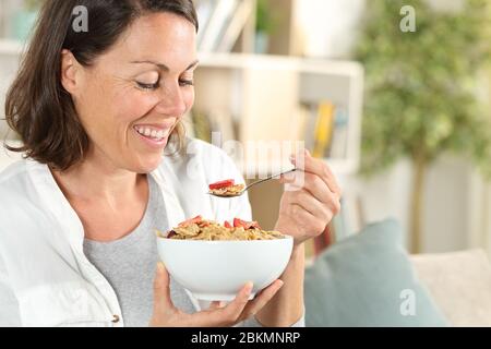 Glückliche Erwachsene Frau, die Müsli Schüssel mit Frühstück auf dem Sofa zu Hause sitzen Stockfoto