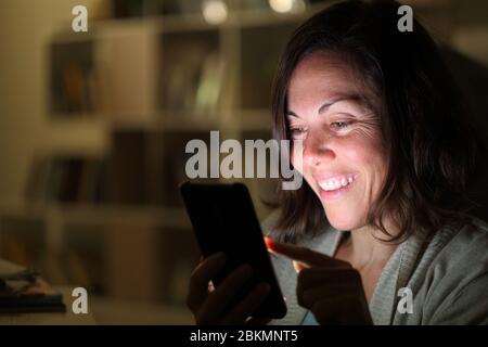 Glückliche Frau mittleren Alters mit Smartphone mit beleuchteten Bildschirm in der Nacht zu Hause Stockfoto