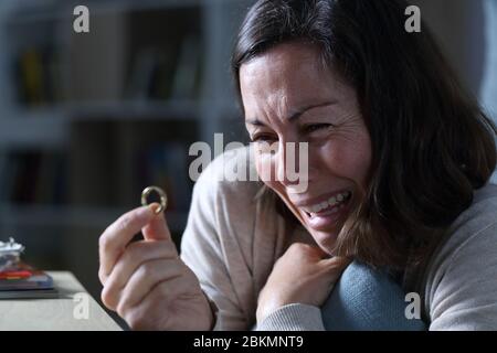 Traurige Frau weinend beim Blick auf Ehering, der in der Nacht zu Hause auf dem Boden sitzt Stockfoto