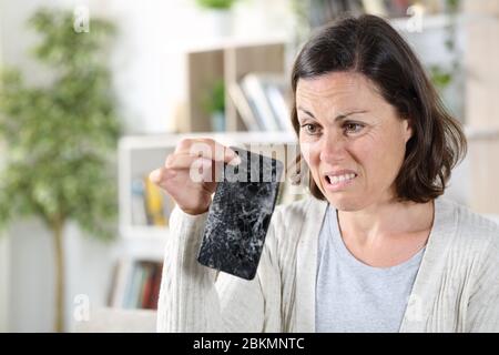Verwirrt Erwachsene Frau Blick auf gebrochene Smartphone mit zerbrochenen Bildschirm zu Hause Stockfoto