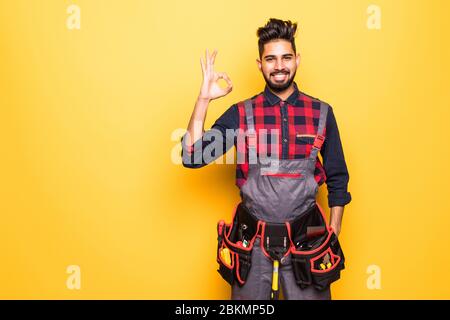 Indischer Mann Arbeiter trägt harten Hut und mit OK Zeichen auf gelbem Hintergrund Stockfoto