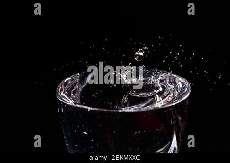 Schwarzer Hintergrund ist ein Glas, in das ein Tropfen Wasser fällt. Spritzwasser auf Glas Stockfoto