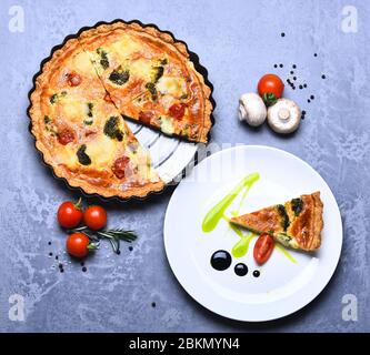 Vegetarische Pizza mit Tomaten, Brokkoli und Käse auf grauem Hintergrund. Veganes Essen im Café oder Restaurant. Traditionelle rustikale Küche. Pizza Pie in Metall Backform in der Nähe Stück auf Teller serviert Stockfoto