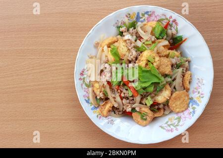 Bild von oben. Gebratener Tofu mit Schweinefleisch, Zwiebeln, Sellerie, Koriander und etwas frischem Chili umrühren. In einen weißen Teller mit Blumenmuster legen und platzieren Stockfoto