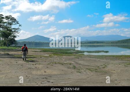 Ein Mann, der vor einem Berghintergrund am See entlang wandert, Lake Elementaita, Kenia Stockfoto