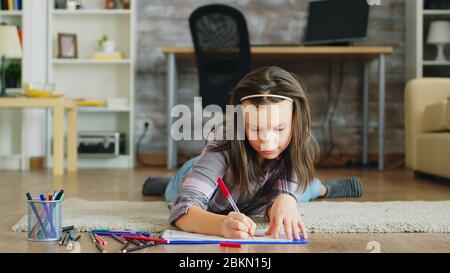 Fröhliches kleines Mädchen, das auf dem Boden liegt und eine kreative Zeichnung macht. Stockfoto