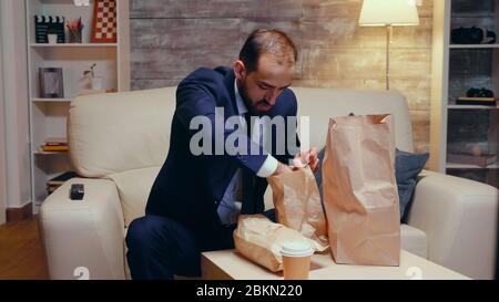 Folgen Sie dem Bild eines hungrigen Geschäftsmannes, der mit Essen zum Mitnehmen nach Hause kommt. Stockfoto