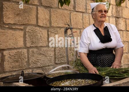 Konavle, Kroatien, 5. September 2019. Eine ältere Frau, die ein tranditional altes Folklore-Kostüm trägt und typische kroatische Oliven mit Salz und einem macht Stockfoto