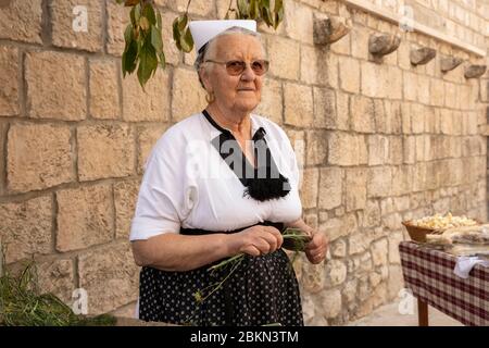 Konavle, Kroatien, 5. September 2019. Ein Porträt einer älteren Frau, die ein tranditional alten Folklore-Kostüm trägt und typische kroatische Oliven wi Stockfoto