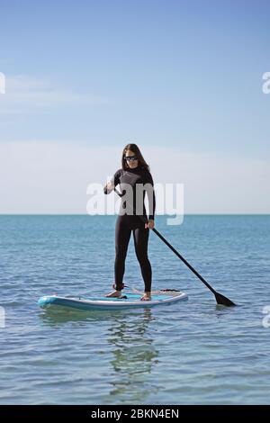 Junge Frau Stand Up Paddle Boarding im blauen Meer Stockfoto