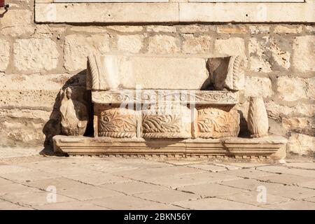 Eine Bank in Korcula auf dem Hauptplatz vor der Kathedrale St. Marks. Diese Bank ist aus Kalkstein aus verschiedenen alten Elementen zusammengesetzt Stockfoto