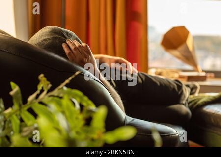 Ein Mann, der eine flache Mütze trägt, entspannt und ein Nickerchen macht, während er drinnen auf der Couch bleibt, einen sonnigen Tag in einem Retro, Vintage, eklektischem Stil mit oder Stockfoto