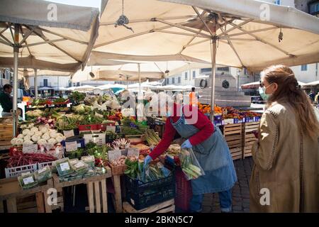 Der Verkäufer, der eine schützende Gesichtsmask trägt, bedient einen Kunden am Montag, den 4. Mai 2020, auf dem Obst- und Gemüsemarkt am Campo dei Fiori in Rom. Stockfoto