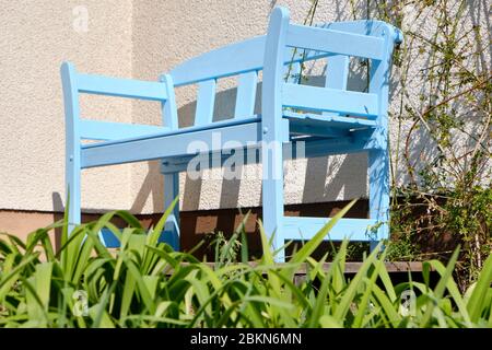 Schöne Holzgartenbank in hellblau lackiert, die an einem sonnigen Frühlingstag vor einer Hauswand auf einer Terrasse steht. Gesehen in Deutschland im April Stockfoto