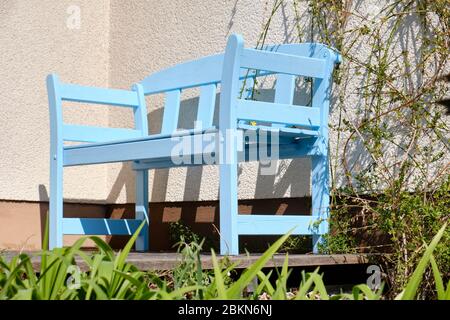 Schöne Holzgartenbank in hellblau lackiert, die an einem sonnigen Frühlingstag vor einer Hauswand auf einer Terrasse steht. Gesehen in Deutschland im April Stockfoto