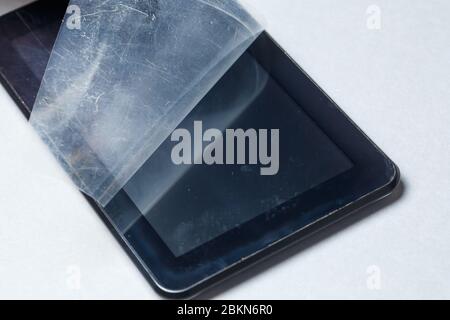 Schwarz verkratztes Tablett mit einer Schutzfolie auf grauem Hintergrund. Schützen Sie den Bildschirm Ihres Geräts Stockfoto