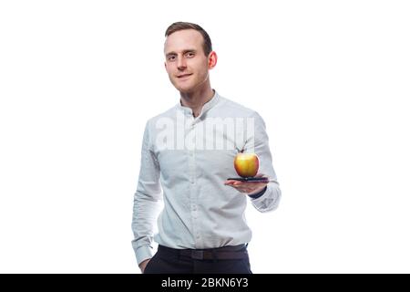 Kaukasischer männlicher Geschäftsmann, der ein Handy in Schwarz hält und einen rot-gelben apfel hält. Er trägt ein Hemd. Emotionales Porträt. Isoliert auf Whit Stockfoto