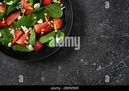 Nahaufnahme von Erdbeersalat mit Spinat auf schwarzem Hintergrund Stockfoto