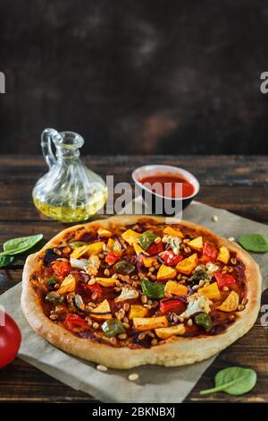 Vertikale Aufnahme von veganer Pizza aus Eigenbau mit Gemüse, Pesto und Pinienkernen Stockfoto