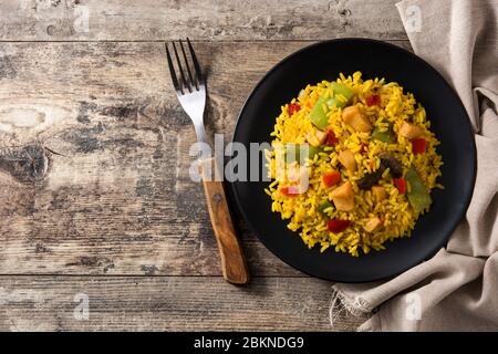 Gebratener Reis mit Huhn und Gemüse auf schwarzem Teller auf Holztisch. Draufsicht. Kopierbereich Stockfoto