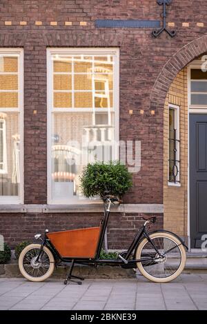 Typisch holländisches Fahrrad vor einem Haus geparkt. Moderne städtische Eltern nutzen diese Trägerräder, um ihre Lebensmittel oder Kinder zu transportieren Stockfoto