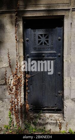 Kunstvolle rostige Metall geschlossene Tür in alten Krypta Grab des Friedhofs in Paris Frankreich. Verwitterte staubige Steinwand von Efeu Kletterpflanze mit trockenen überwuchert Stockfoto