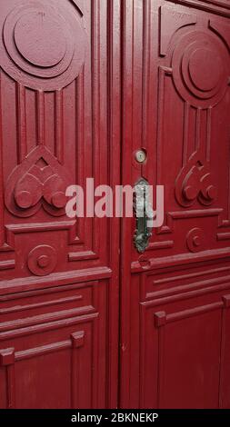 Gemusterte Rahmen aus roten Doppeltürverkleidungen der antiken Tür mit skulpturalen Vintage Türgriff. Rot bemalte verzierte Holztüren Stockfoto