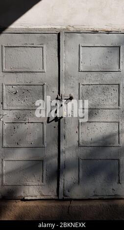 Grunge Doppeltür aus Scheune Holzpaneelen mit abblätternder Farbe und Schatten in hellem Sonnenlicht. Raue Oberfläche der alten grauen Tür mit verschwommenen Schatten Stockfoto